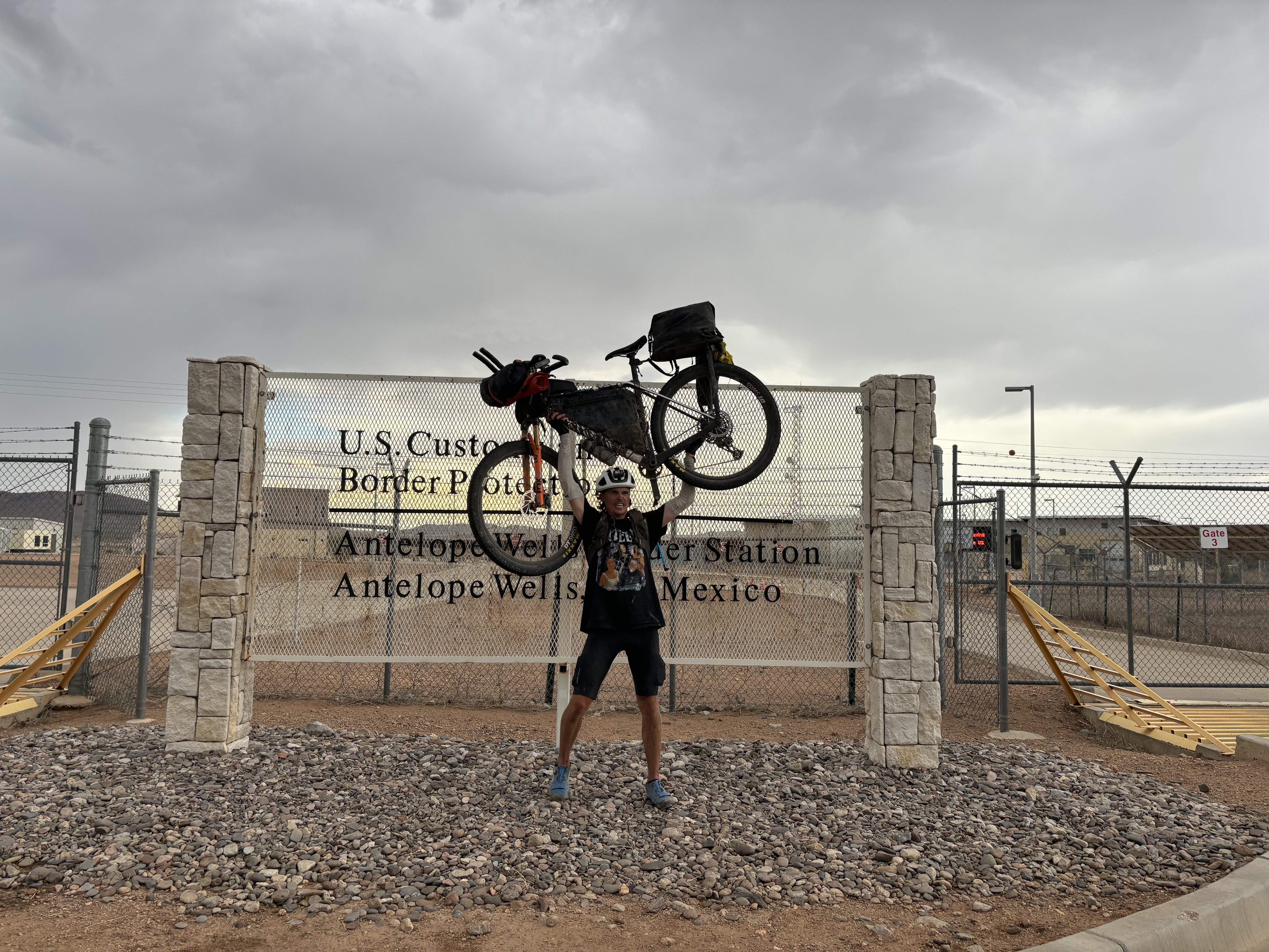 Bikepacker riding toward mountain walls on a paved road.